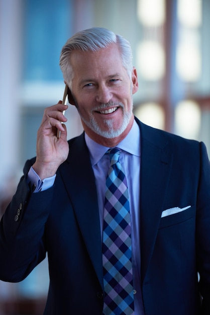 hombre de negocios senior habla por teléfono móvil en el interior de la oficina moderna y luminosa