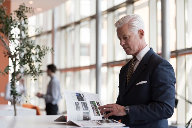 hombre de negocios senior leyendo una revista en una oficina moderna y luminosa