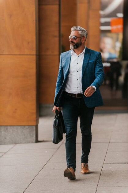 El hombre de negocios senior moderno con una bolsa sale de la corporación moderna.