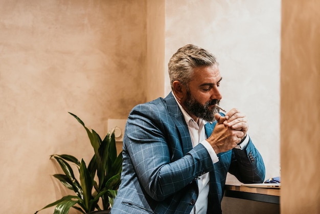 Un hombre de negocios senior moderno fuma un cigarrillo mientras descansa en un café después de un duro día de trabajo