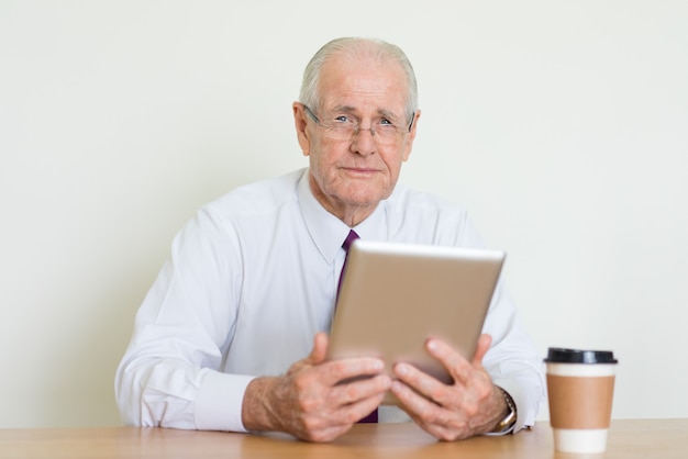 hombre de negocios senior serio mirando a cámara y usando la tableta a