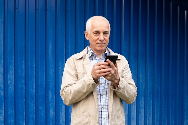 Hombre de negocios senior con smartphone en fondo azul, copyspace. Hombre mayor, tecnología moderna