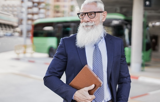 Hombre de negocios senior sosteniendo tableta digital en la ciudad con la estación de autobuses en segundo plano.