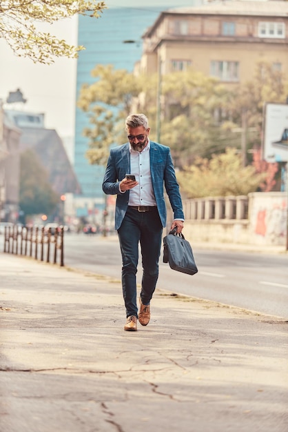 Un hombre de negocios senior con traje azul en un entorno urbano usando un teléfono inteligente.