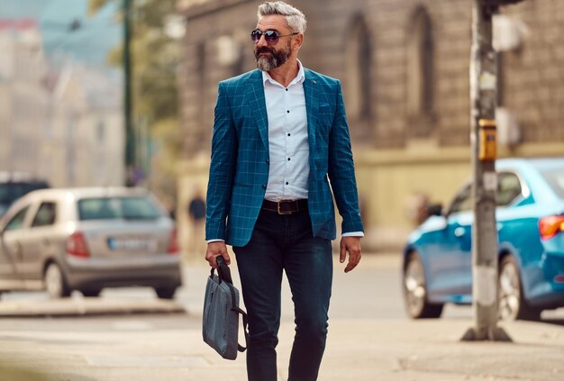 Un hombre de negocios senior con traje azul y maletín caminando por la ciudad.