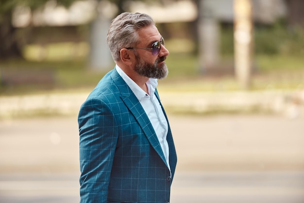 Un hombre de negocios senior con traje azul y maletín caminando por la ciudad.