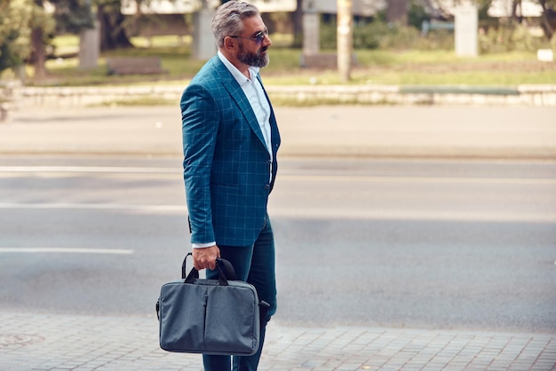 Un hombre de negocios senior con traje azul y maletín caminando por la ciudad.