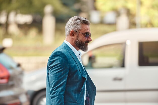 Un hombre de negocios senior con traje azul y maletín caminando por la ciudad.