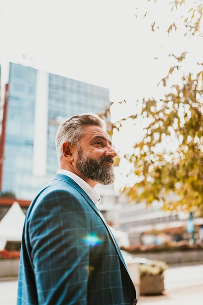 Un hombre de negocios senior con traje caminando por la ciudad después del trabajo