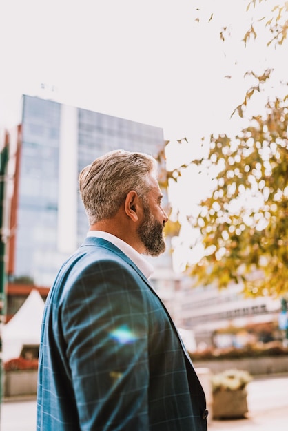 Un hombre de negocios senior con traje caminando por la ciudad después del trabajo.