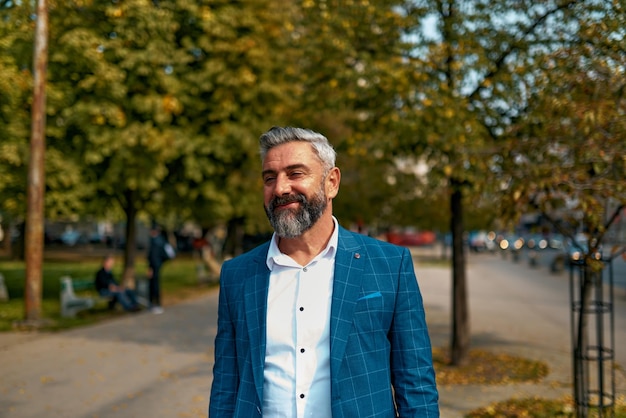 Un hombre de negocios senior con traje caminando por la ciudad después del trabajo.