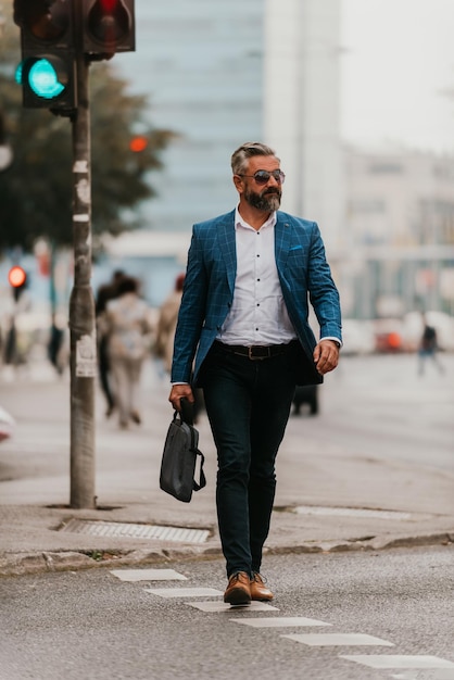 Un hombre de negocios senior con traje y gafas de sol caminando por la ciudad mientras lleva una bolsa