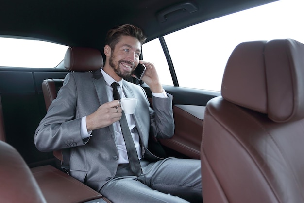 hombre de negocios, sentado, en coche, con, taza, y, teléfono inteligente