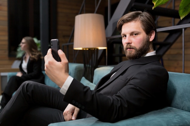 Hombre de negocios sentado en un elegante restaurante en un traje de negocios relajante y utiliza el teléfono para comunicarse