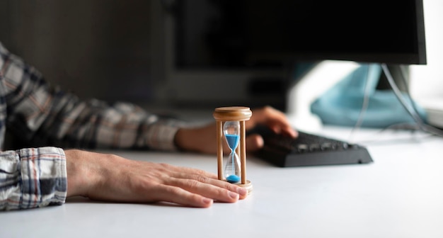 Un hombre de negocios sentado en la mano del lugar de trabajo sosteniendo un reloj de arena como el concepto de tiempo es dinero