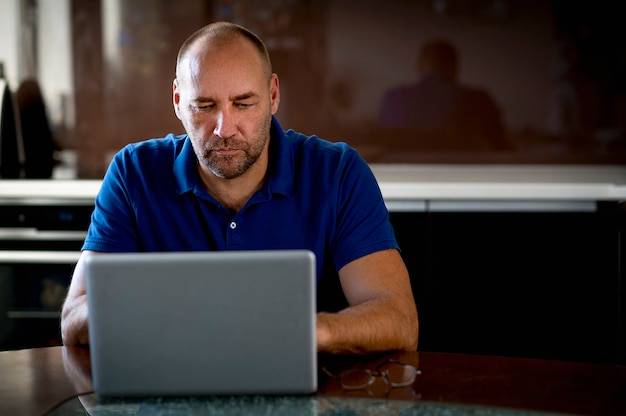 Hombre de negocios sentado en una mesa de comedor y usando una computadora portátil mientras trabaja desde casa