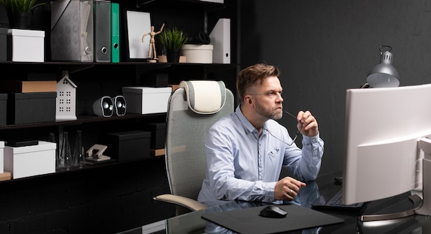 Hombre de negocios sentado en la oficina en el escritorio de la computadora y sosteniendo su boca grillete de gafas
