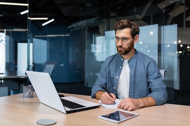 Un hombre de negocios serio está escribiendo información estudiando en línea mientras está sentado dentro de la oficina