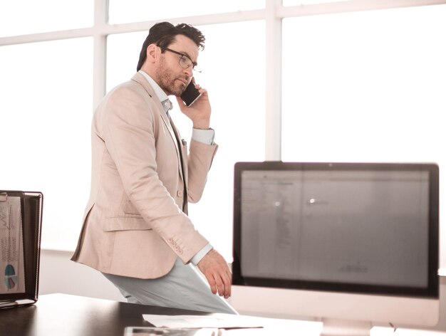 Hombre de negocios serio hablando por teléfono inteligente sentado en su concepto de escritorio