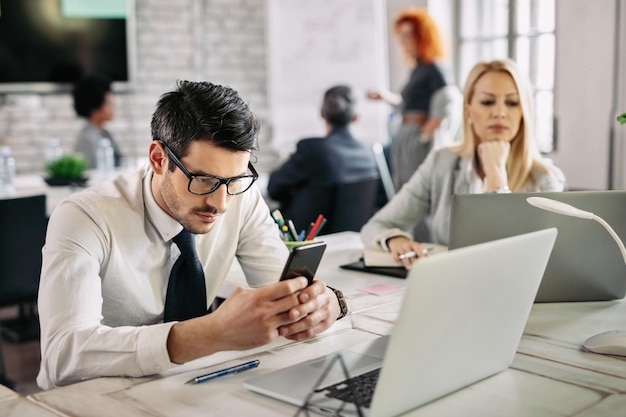 Hombre de negocios serio que lee el mensaje de texto en el teléfono móvil en el trabajo