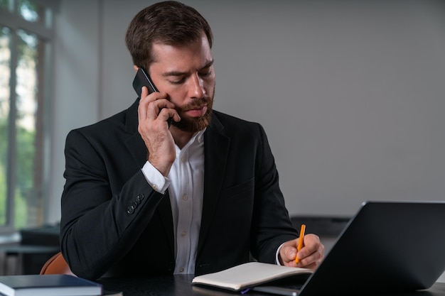 Hombre de negocios serio con traje formal hablando por teléfono inteligente tomando notas