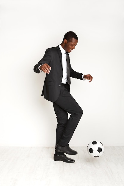 Hombre de negocios serio en traje jugando al fútbol. Hombre afroamericano divirtiéndose con balón de fútbol, aislado sobre fondo blanco.