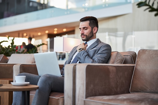 Hombre de negocios serio usando su computadora portátil en el pasillo y frunciendo el ceño