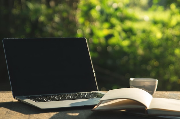 Un hombre de negocios se sienta en un escritorio de madera en el jardín temprano en la mañana usando su computadora portátil para comunicarse con otros tomando café mientras navega por Internet en el área al aire libre