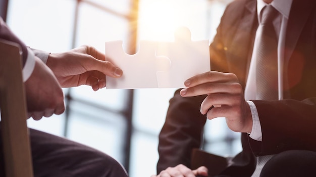 Un hombre de negocios se sienta en una mesa y sostiene una pieza de rompecabezas como símbolo de una decisión empresarial y un concepto empresarial exitoso