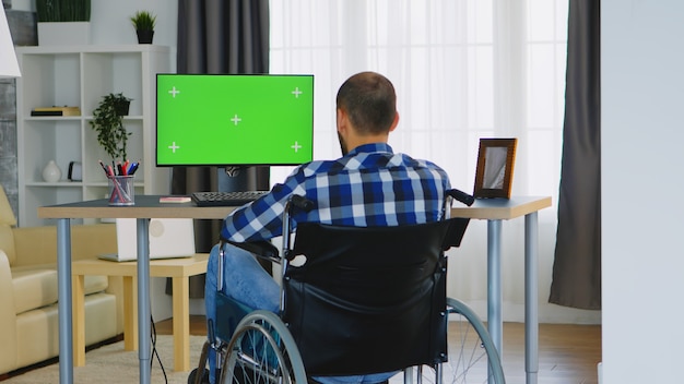 Hombre de negocios en silla de ruedas frente a computadora con pantalla verde.