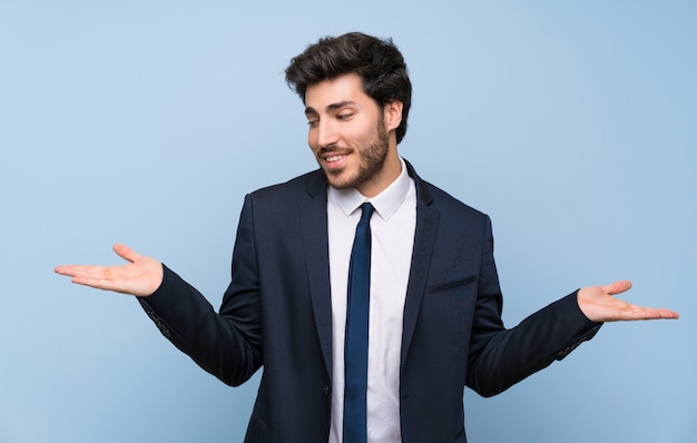 Hombre de negocios sobre la pared azul aislada que sostiene el copyspace con dos manos