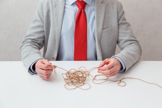 El hombre de negocios solo intenta desenrollar la bola de hilo enredado como una situación de rompecabezas. Fotografía conceptual. No cara. El hombre encuentra una salida a la situación por sí mismo