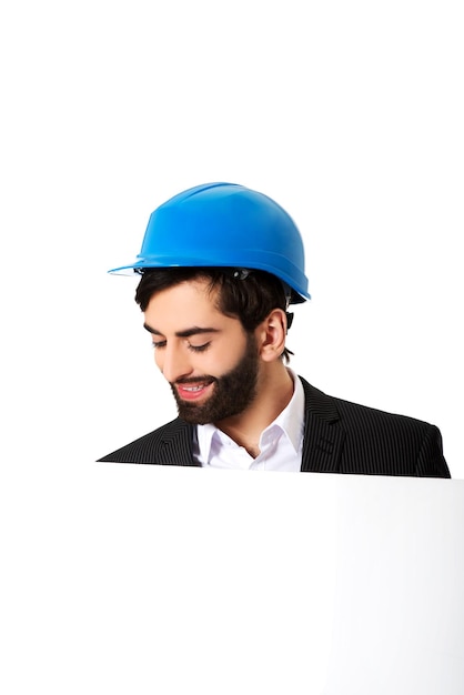 Hombre de negocios con sombrero azul mirando un cartel en blanco contra un fondo blanco