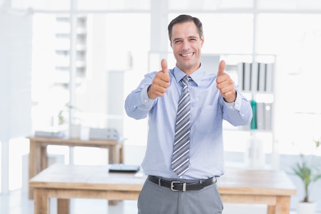 Hombre de negocios sonriendo a la cámara con los pulgares arriba