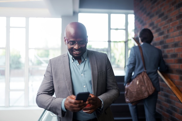 Hombre de negocios sonriendo. Empresario barbudo de piel oscura con gafas sonriendo mientras lee el mensaje