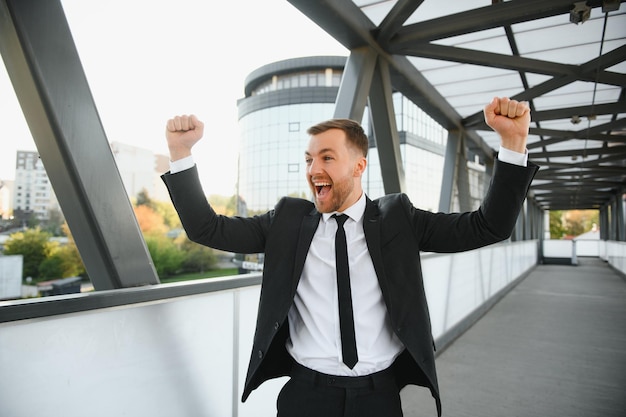 Hombre de negocios sonriendo y levantando el puño en el aire con el logro del éxito empresarial de fondo del edificio de oficinas y ganar conceptos