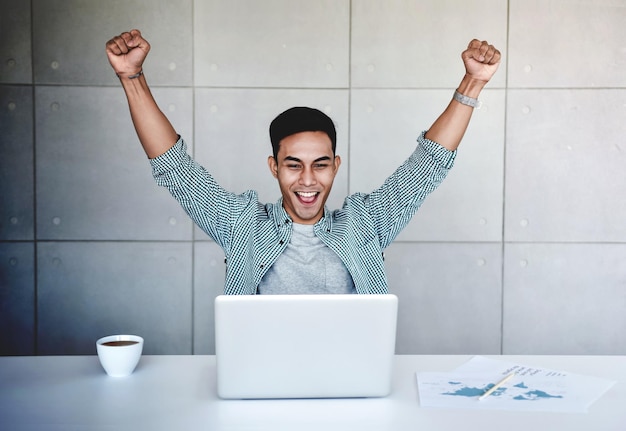 Un hombre de negocios sonriente apretando los puños mientras usa una computadora portátil en la oficina