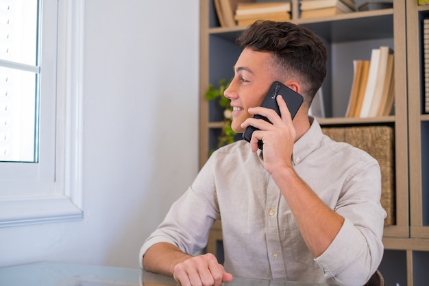 Hombre de negocios sonriente con gafas hablando por teléfono, sentado en el escritorio con una computadora portátil, gerente amable que consulta al cliente por teléfono, hombre feliz charlando con amigos distraídos del trabajo