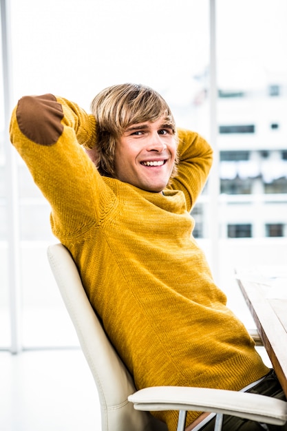 Hombre de negocios sonriente del inconformista que se sienta en su escritorio y que mira la cámara