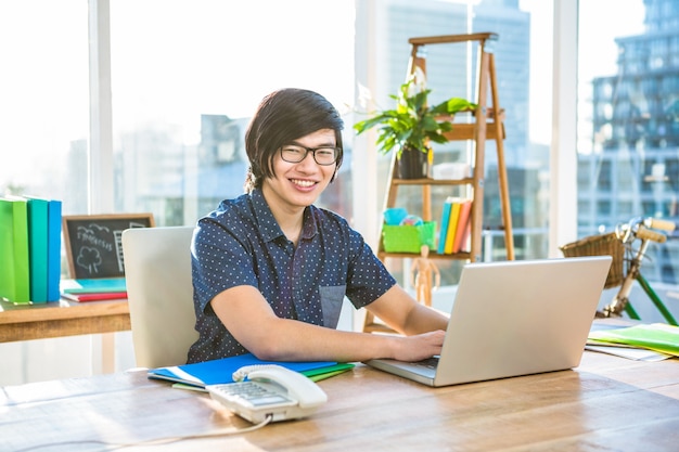 Hombre de negocios sonriente del inconformista que usa el ordenador portátil en oficina