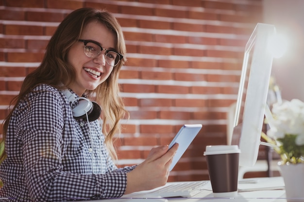 Hombre de negocios sonriente del inconformista que usa la tableta en su escritorio en oficina