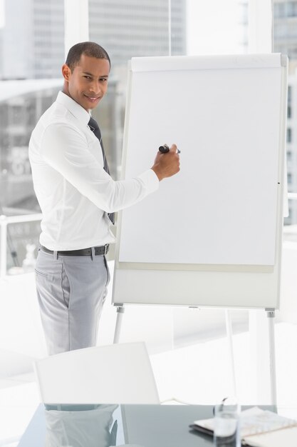 Hombre de negocios sonriente joven que presenta en whiteboard con el marcador