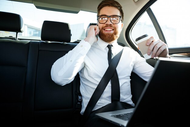 Hombre de negocios sonriente con laptop hablando por teléfono