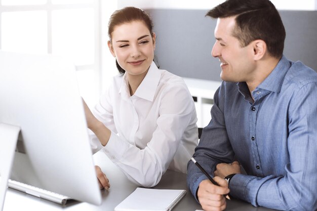 Un hombre de negocios sonriente y una mujer trabajando con una computadora en una oficina moderna. Disparo en la cabeza en la reunión o el lugar de trabajo. Trabajo en equipo, asociación y concepto de negocio.