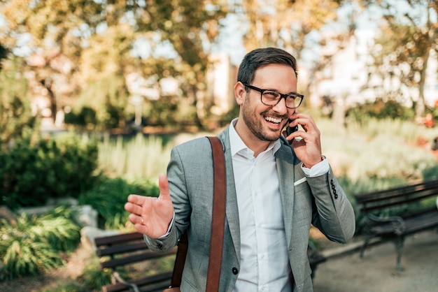 Hombre de negocios sonriente que habla en el teléfono elegante en el parque.