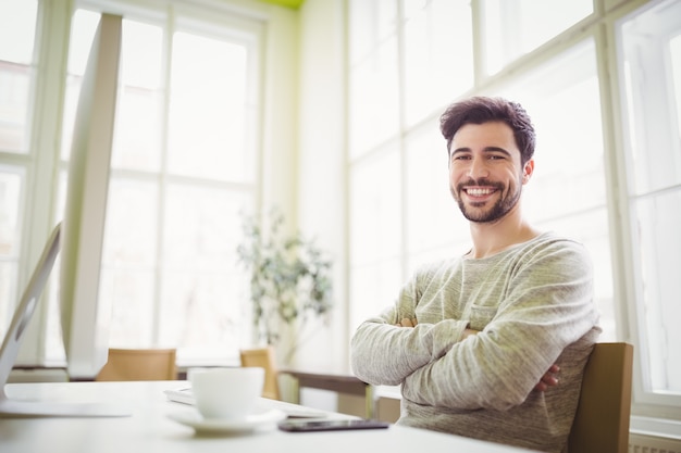 Hombre de negocios sonriente que se sienta en el escritorio en oficina