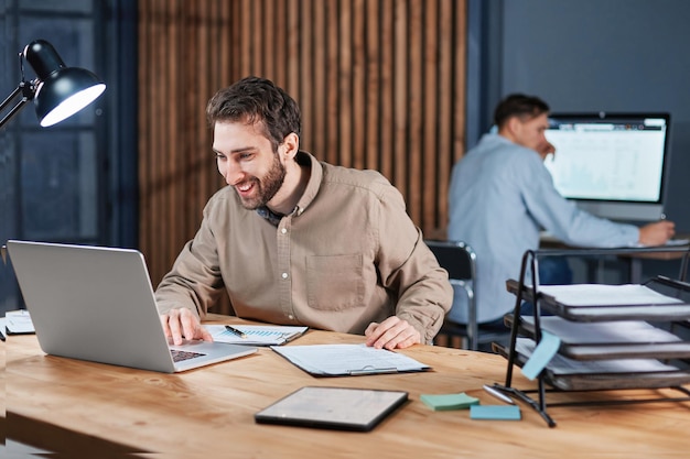 Hombre de negocios sonriente que trabaja en una computadora portátil en una oficina nocturna