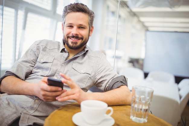 Hombre de negocios sonriente que usa el teléfono móvil en oficina creativa