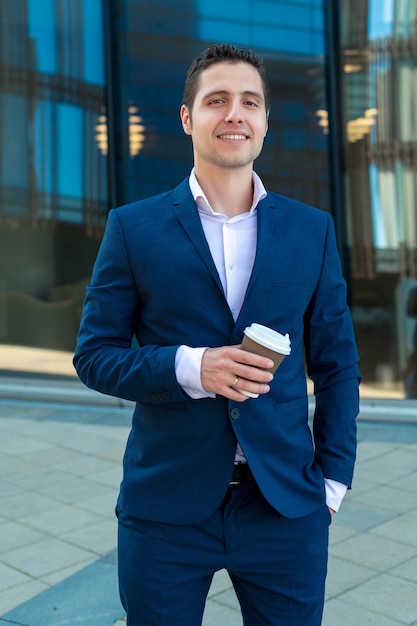 Hombre de negocios sonriente en traje sosteniendo una taza de café en el fondo con rascacielos