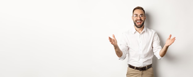 Un hombre de negocios sorprendido y feliz le da la bienvenida luciendo emocionado y sonriente de pie contra el respaldo blanco